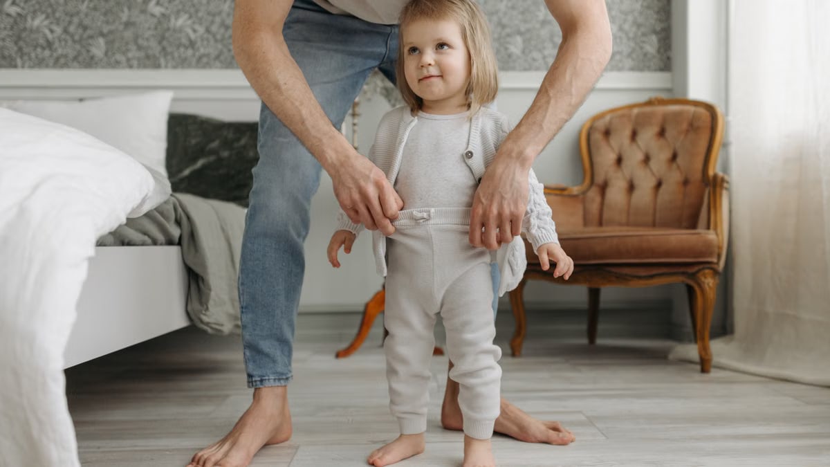 Father helping toddler child get dressed in a cozy bedroom environment.